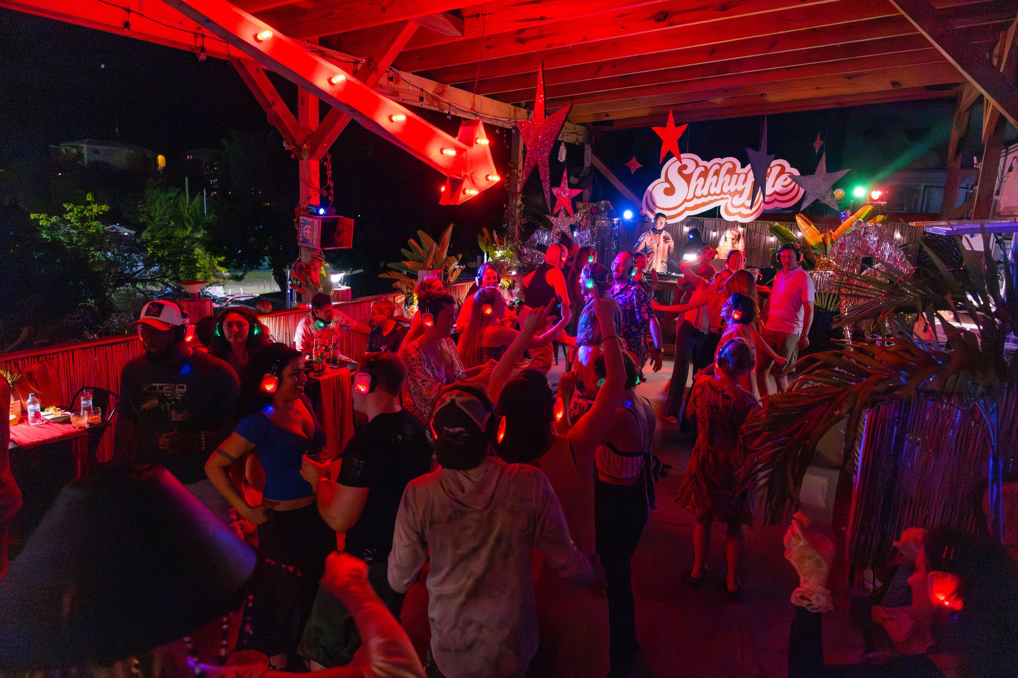 The Speakeasy Shhhuffle silent disco event in St. John, U.S. Virgin Islands — Shhhuffle marquee sign, red lighting, star decor, palm fronds, and a packed dance floor of guests in LED wireless headphones